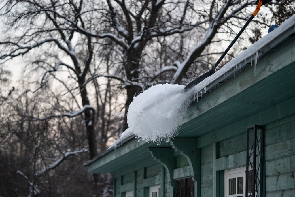 Homeowner removing snow from top of roof in winter