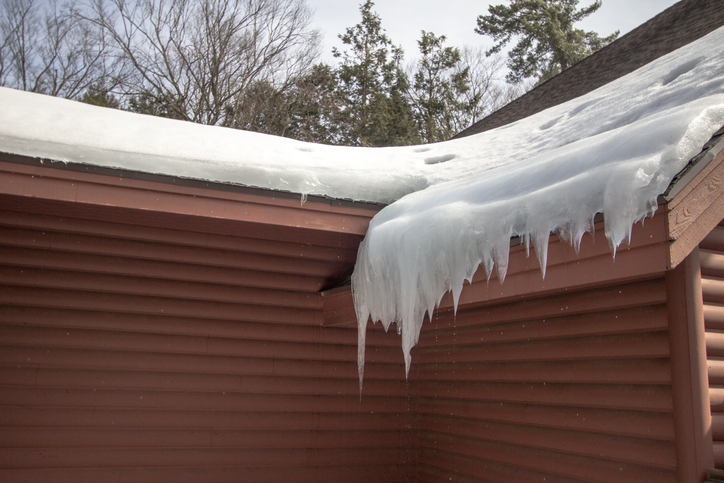 Icicles on a roof with water dripping from below on home exterior.