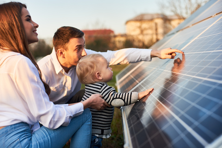 Side close-up shot of a young modern family with a little son getting acquainted with solar panel on a sunny day, green alternative energy concept