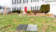 Front yard of house during day aftermath after storm roof tile shingle lying down on grass, damage closeup