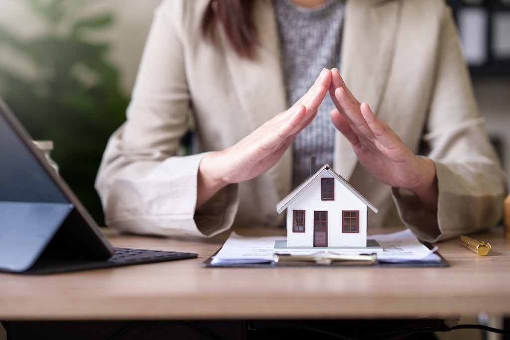 Home insurance agent touching hands together over model house to represent coverage