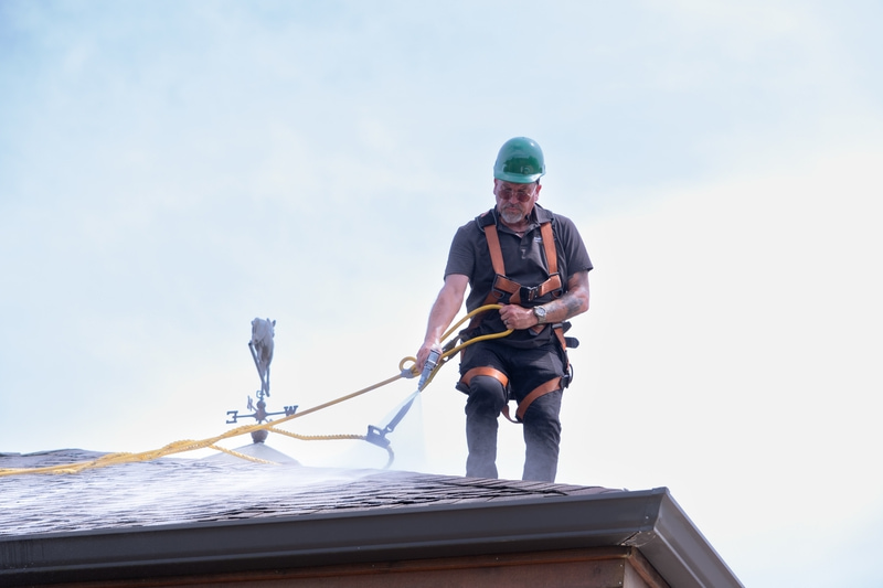 Contractor spraying Roof Maax solution on asphalt shingles of home