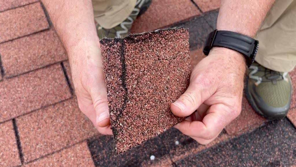Close up shot of a roofer showing a cracked shingle from a brown roof.