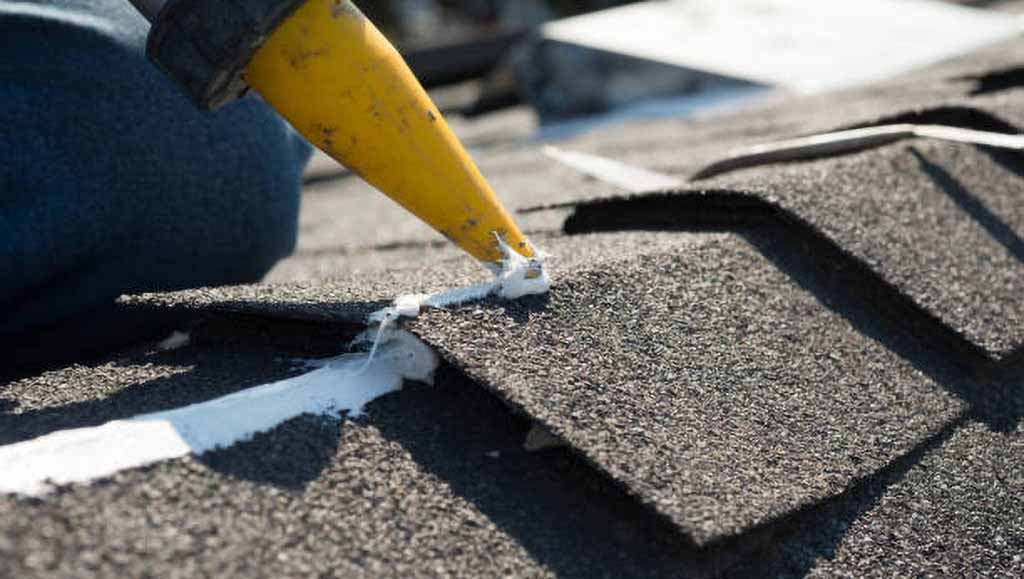 A roofer applies caulking to the ridgeline of a roof.