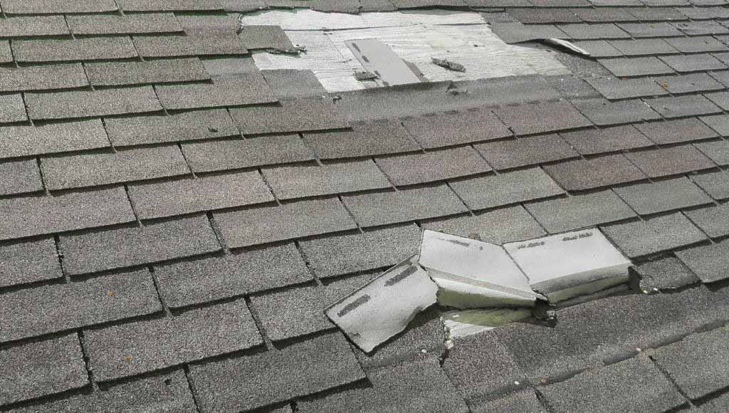 An asphalt shingle roof with large sections of missing shingles