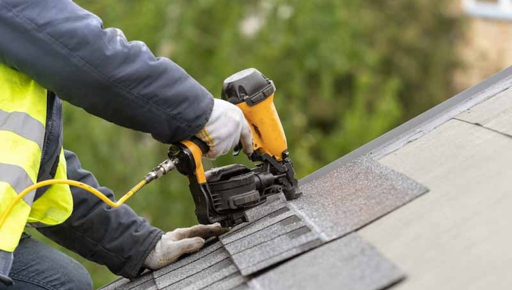 A roofer installs new shingles over a patch of missing shingles.
