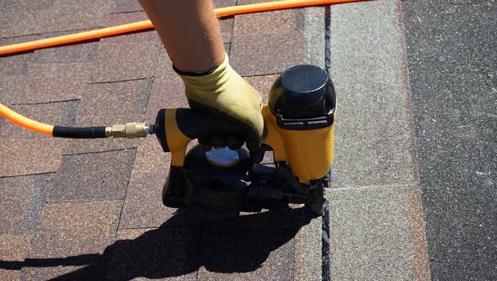 A roofer nailing asphalt shingles with an air gun.