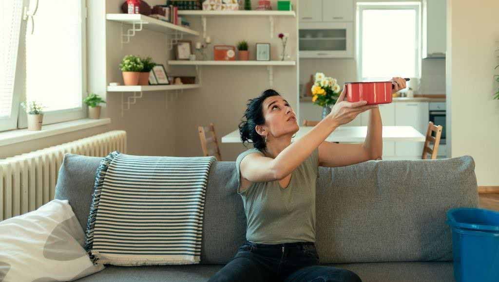 Woman catching water from roof leak in a pot.